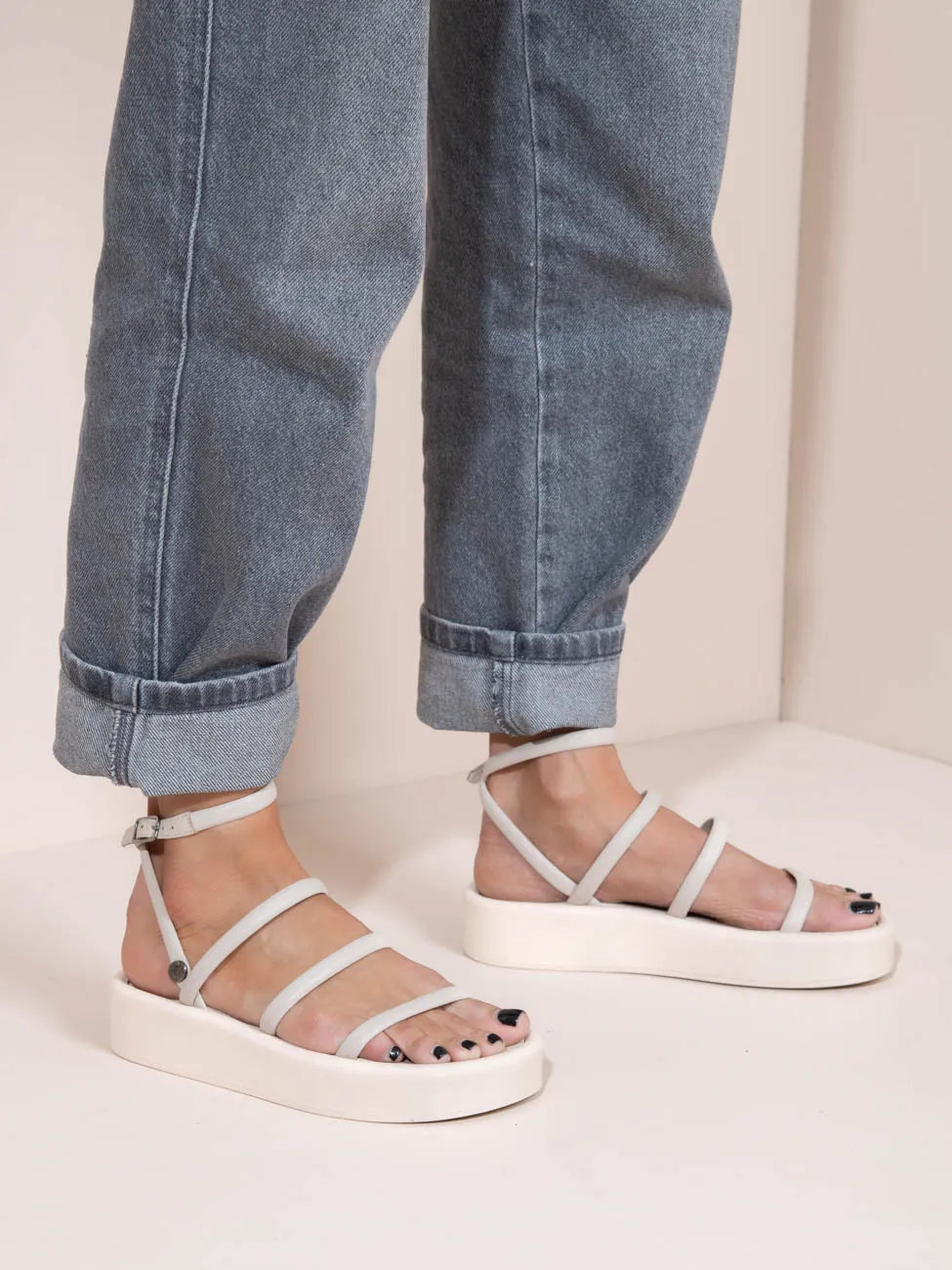 White sandals worn with rolled-up blue jeans on a light background
