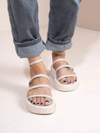 White sandals worn with rolled-up blue jeans on a light background
