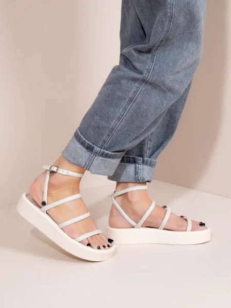 White sandals worn with rolled-up blue jeans on a neutral background