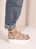 White strappy sandals worn with rolled-up jeans on a neutral background