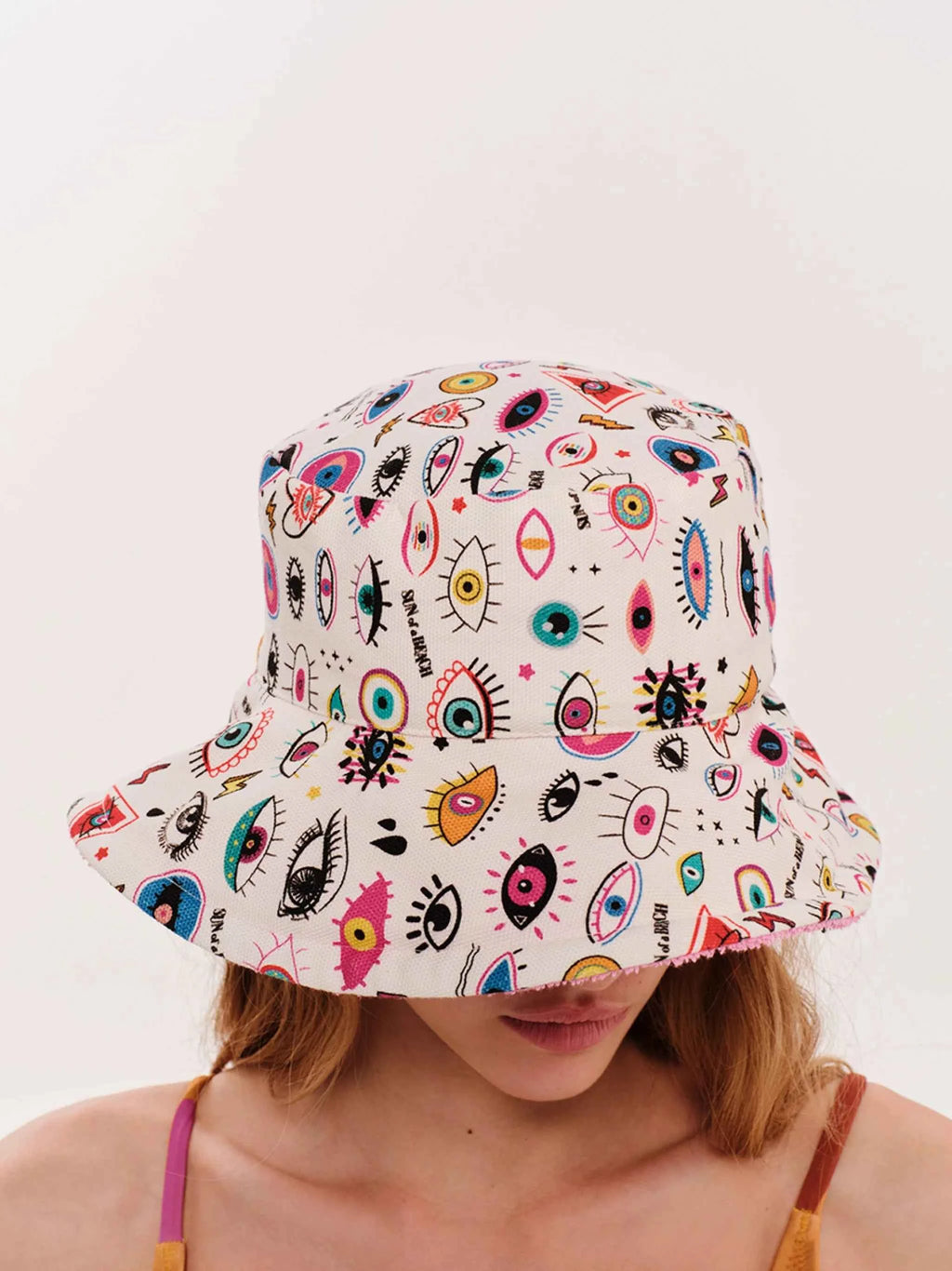 Person wearing a colorful bucket hat with eye pattern on a white background