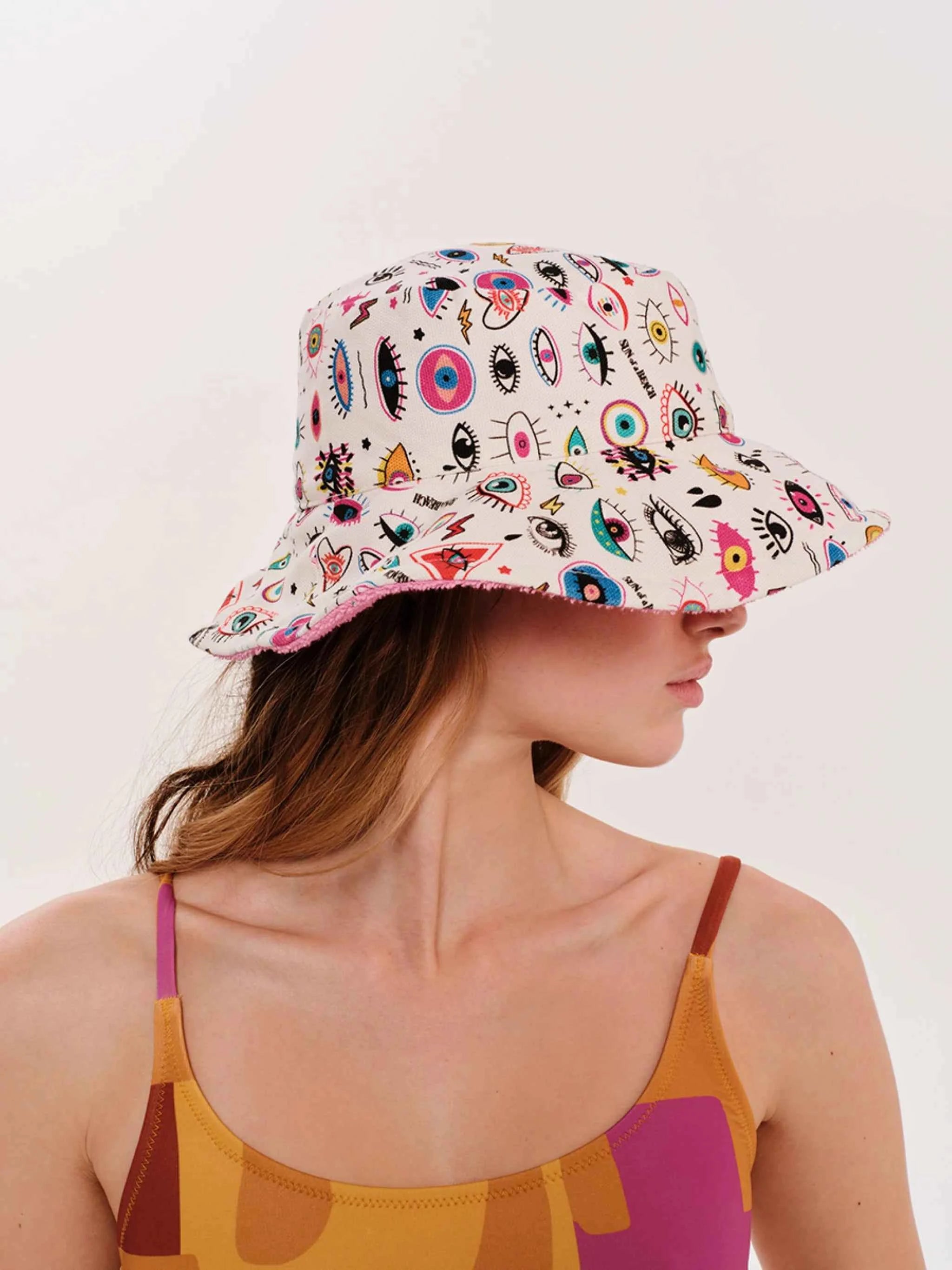 Person wearing a colorful bucket hat with eye designs on a white background