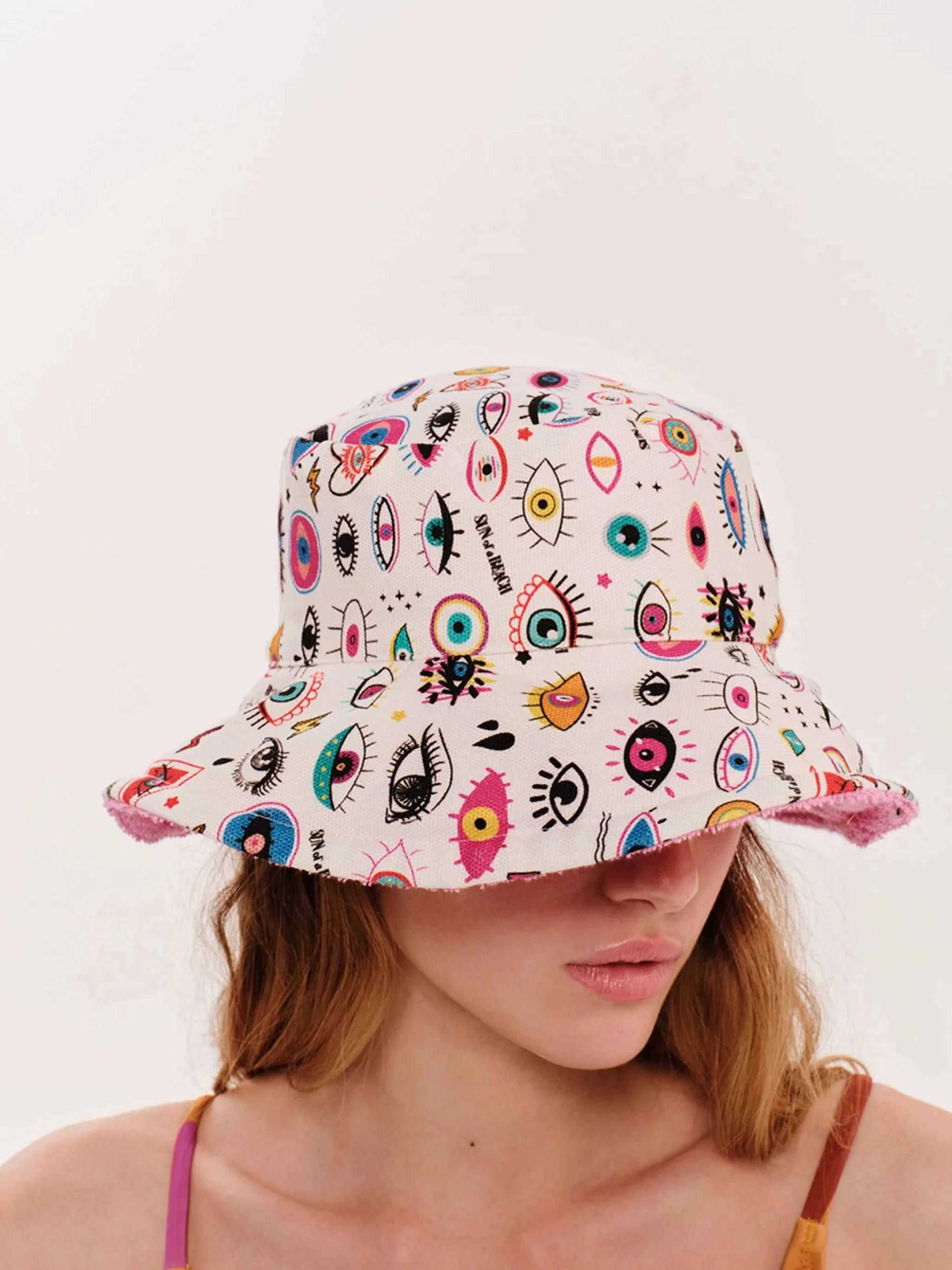 Person wearing a colorful bucket hat with eye designs on a plain background
