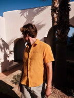Man wearing a mustard yellow shirt standing in front of a white architectural structure with palm trees.