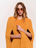 Woman wearing a mustard yellow cape and sunglasses on a plain background