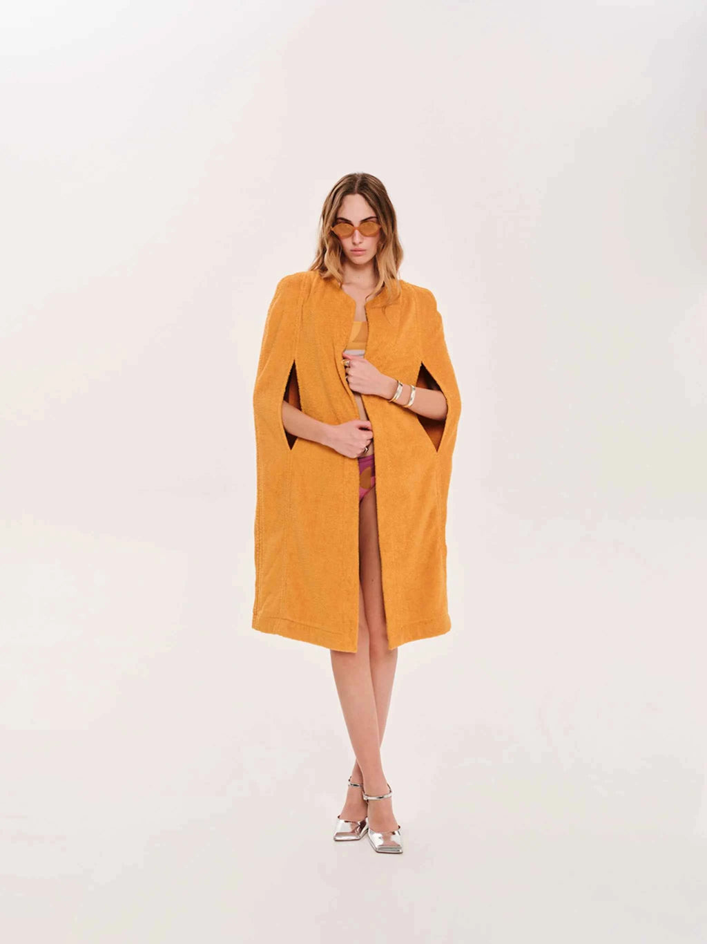 Woman wearing a mustard yellow cape over a dress on a white background