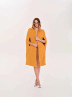 Woman wearing a mustard yellow cape over a dress on a white background