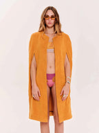 Woman wearing a mustard yellow cover-up and pink bikini on a white background