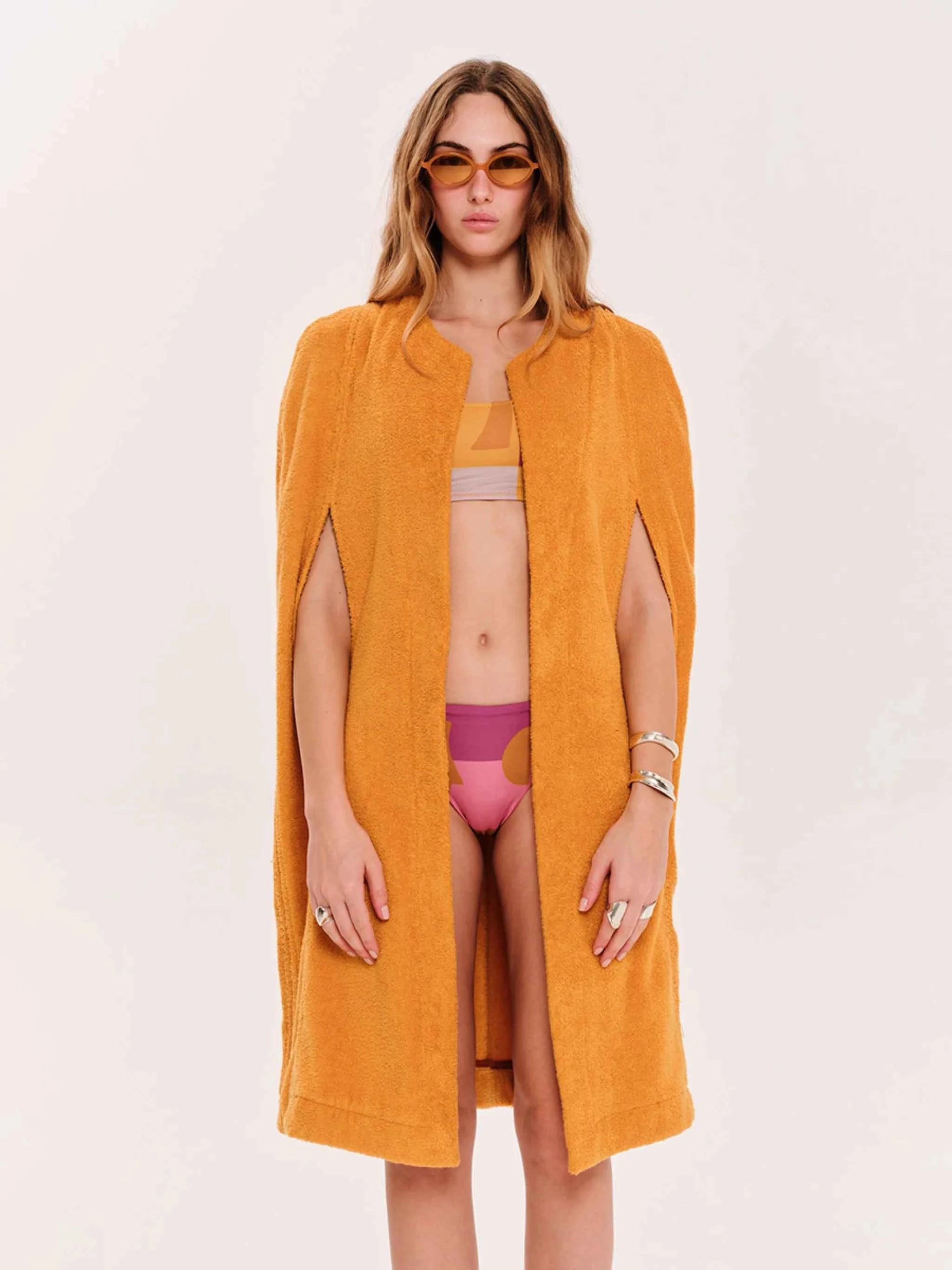 Woman wearing a mustard yellow cover-up and pink bikini on a white background