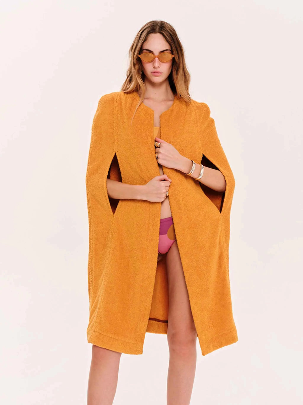 Woman wearing a mustard yellow cape over a pink outfit on a white background