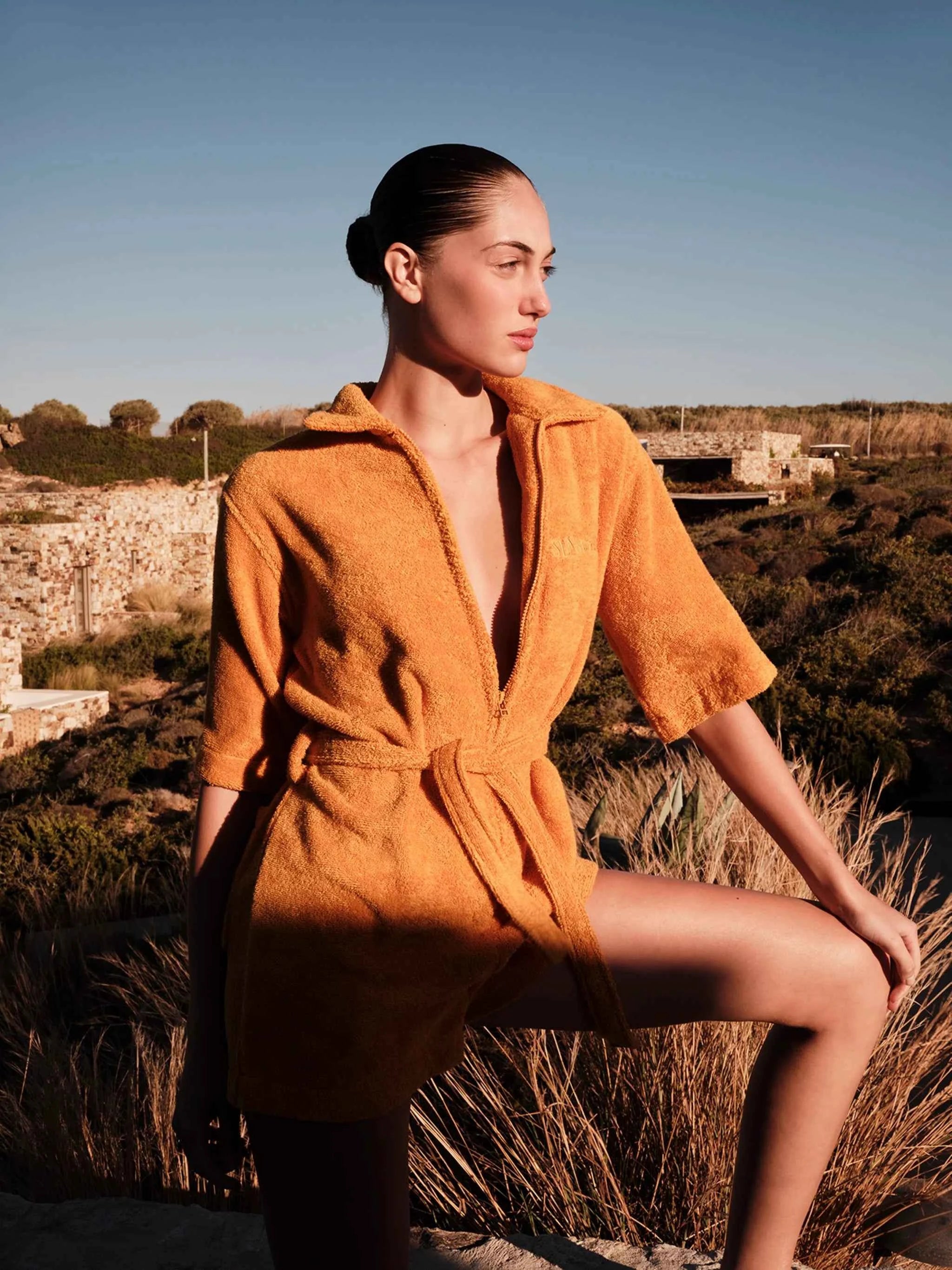 Woman in an orange robe sitting outdoors with a clear blue sky.