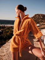 Woman in an orange robe standing by a scenic coastal area.