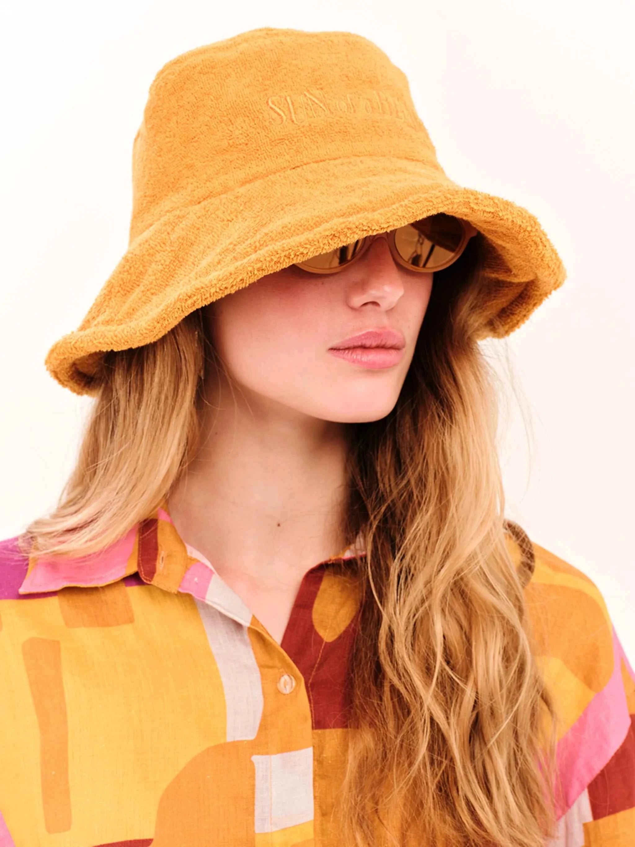 Person wearing a yellow bucket hat and colorful shirt on a white background