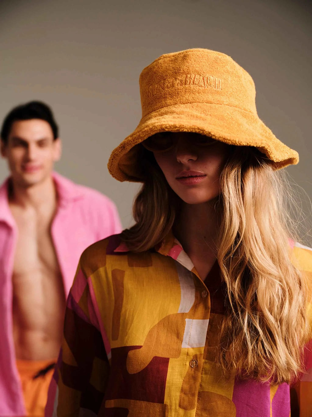 Person wearing a yellow bucket hat with another person in the background.