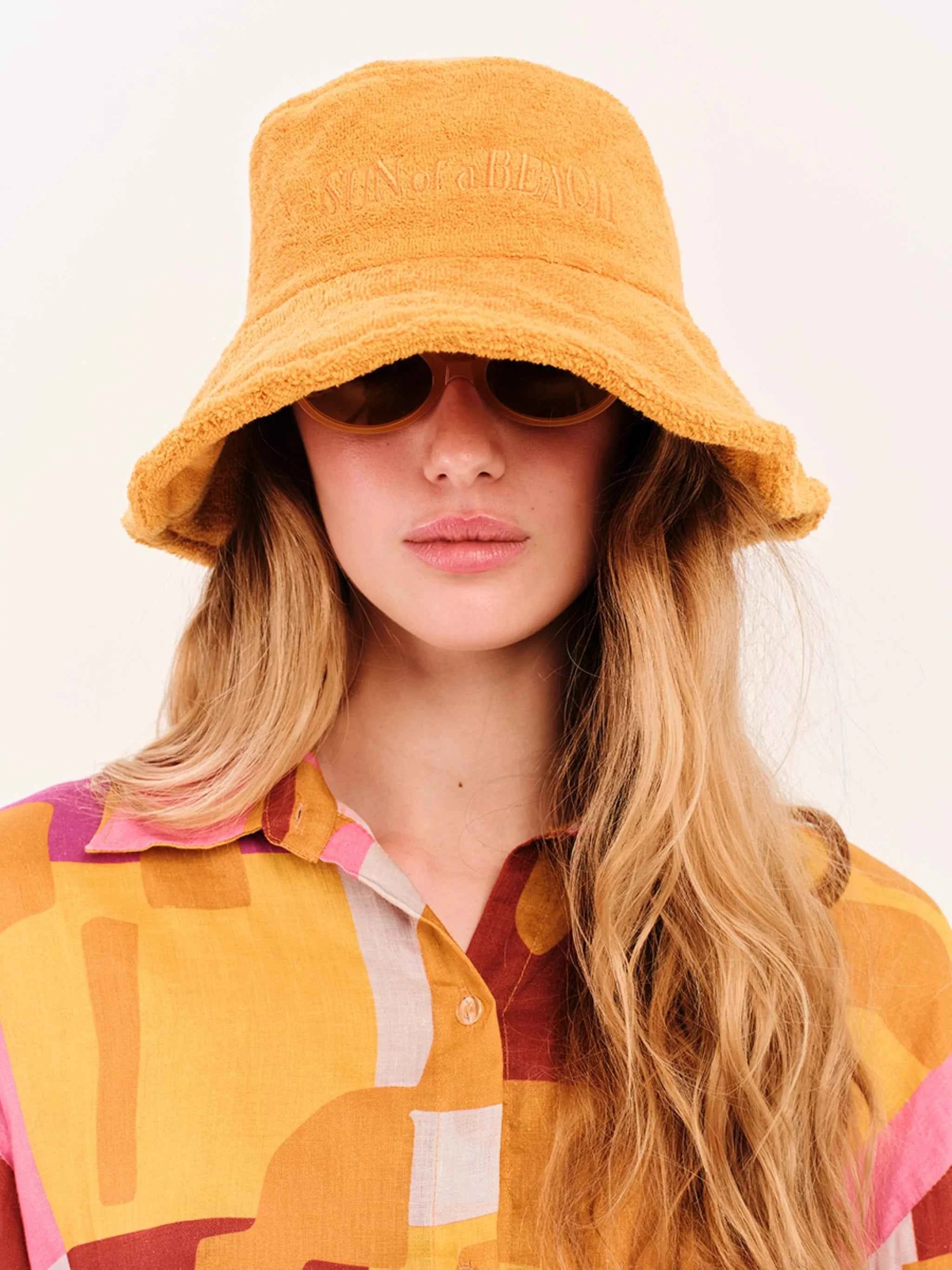 Person wearing a mustard yellow bucket hat with 'The North Face' logo on a white background