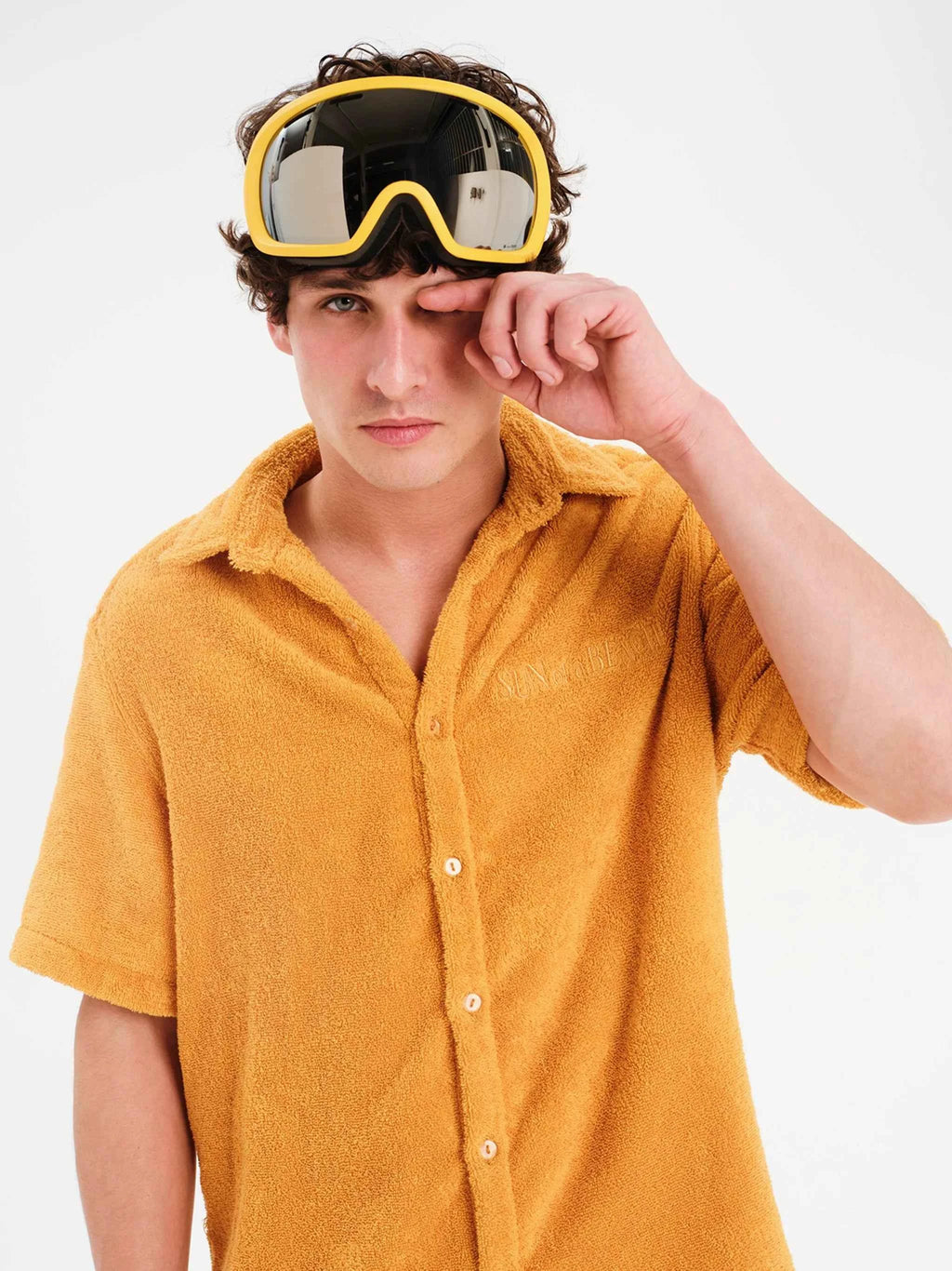 Person wearing mustard yellow shirt and goggles on a white background