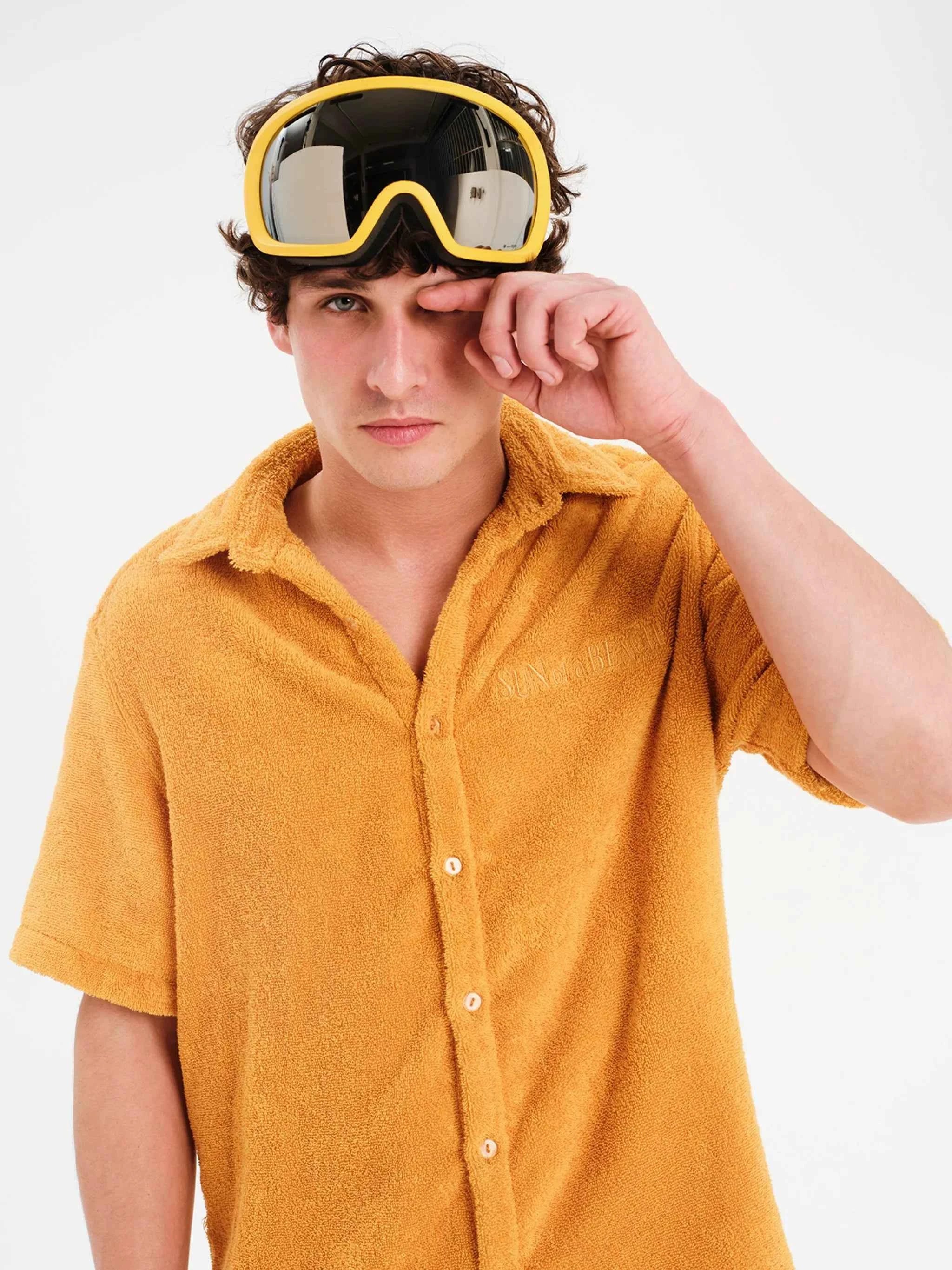 Person wearing mustard yellow shirt and goggles on a white background