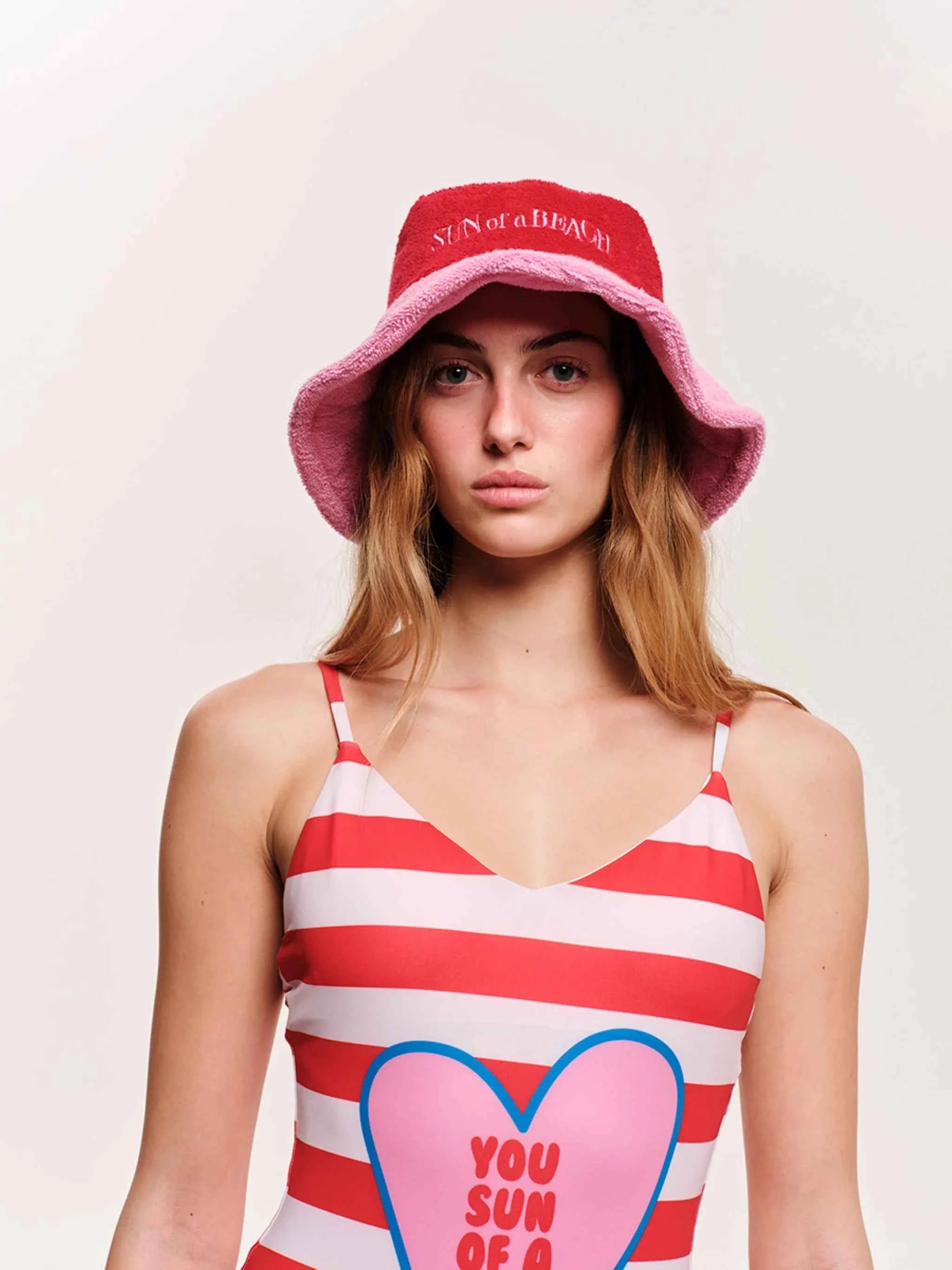 Woman wearing a pink bucket hat and red and white striped dress with a heart design.