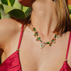Woman wearing a colorful beaded necklace with a red top against a green leafy background