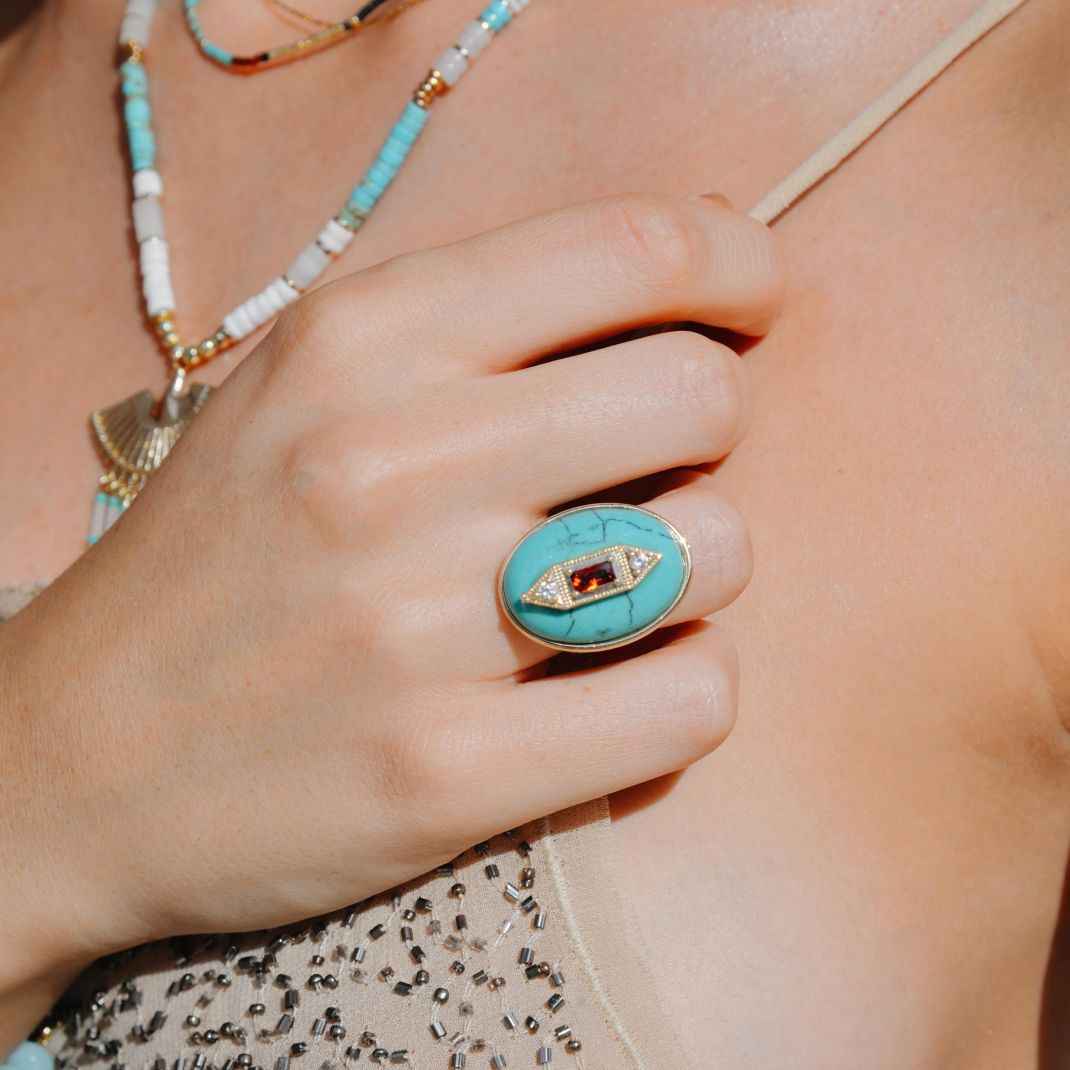Turquoise ring with gemstone worn on a hand, with a necklace in the background