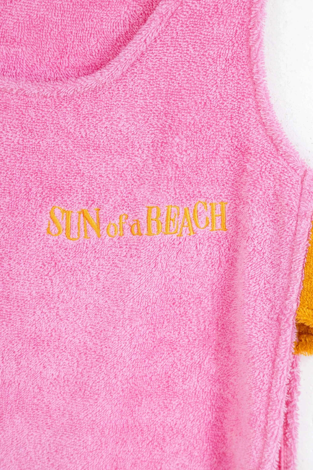 Pink towel with 'SUN of a BEACH' text in gold on a white background