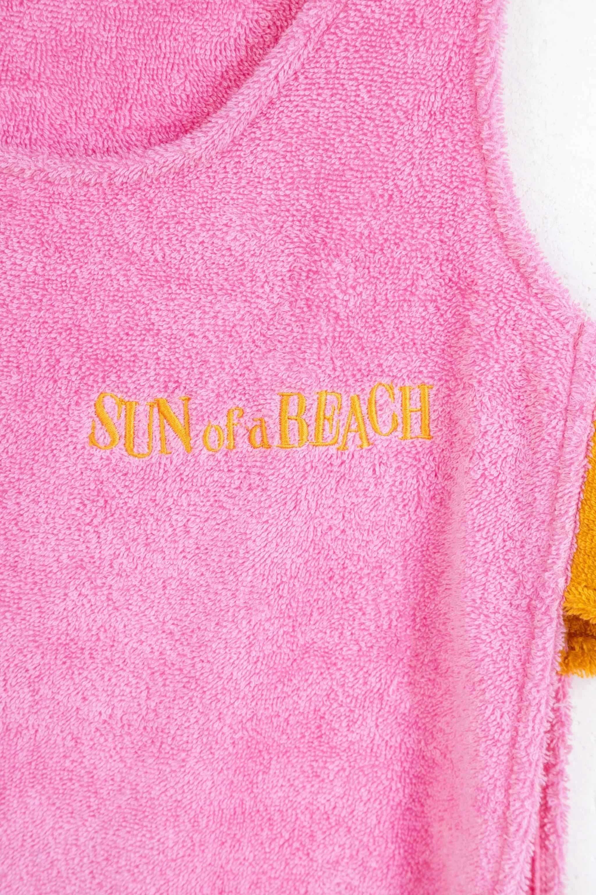 Pink towel with 'SUN of a BEACH' text in gold on a white background
