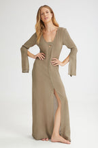 Woman wearing a long, khaki dress with a slit on a white background