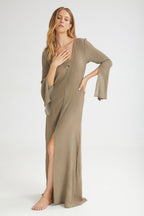 Woman wearing a long, khaki dress with a slit on a white background