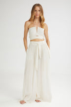 Woman wearing a white halter top and flowing white pants on a white background