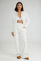 Woman wearing a white outfit with a jacket and pants on a plain background