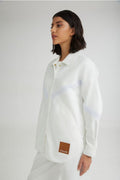 Person wearing a white shirt with a brand patch on a plain background