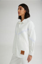 Person wearing a white shirt with a brand patch on a plain background