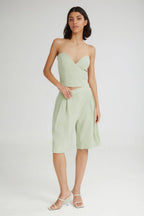 Woman wearing a light green strapless top and high-waisted shorts on a white background