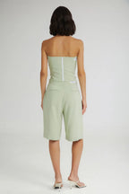 Woman wearing a light green strapless top and shorts on a white background