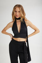 Woman wearing a black halter top and pants with a plain background