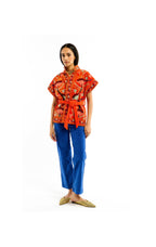 Woman wearing an orange patterned top and blue pants on a white background
