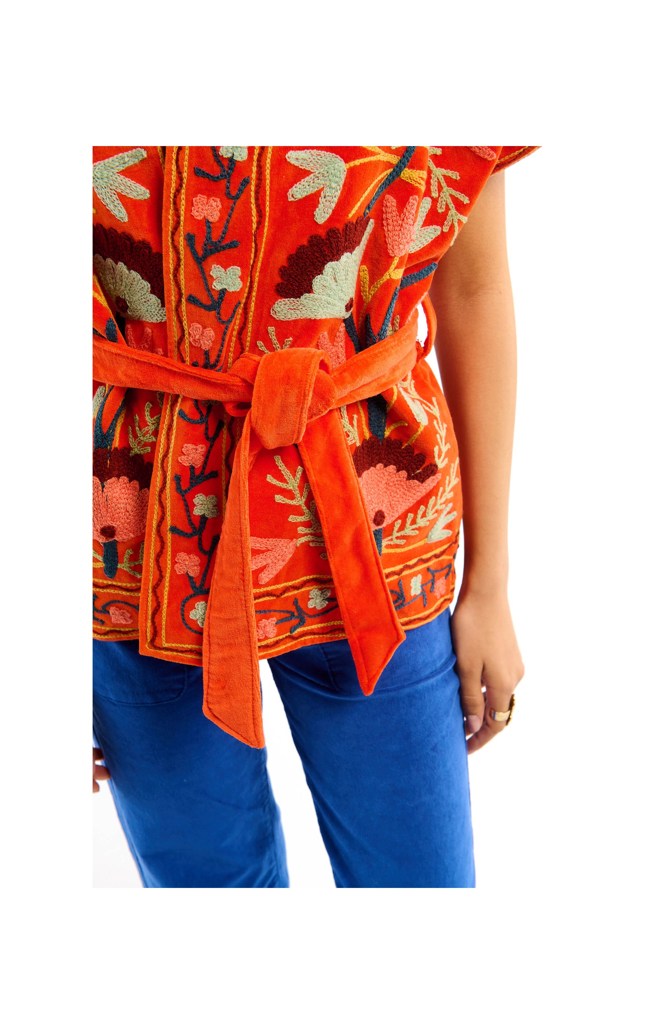 Orange embroidered top with a belt and blue pants on a white background