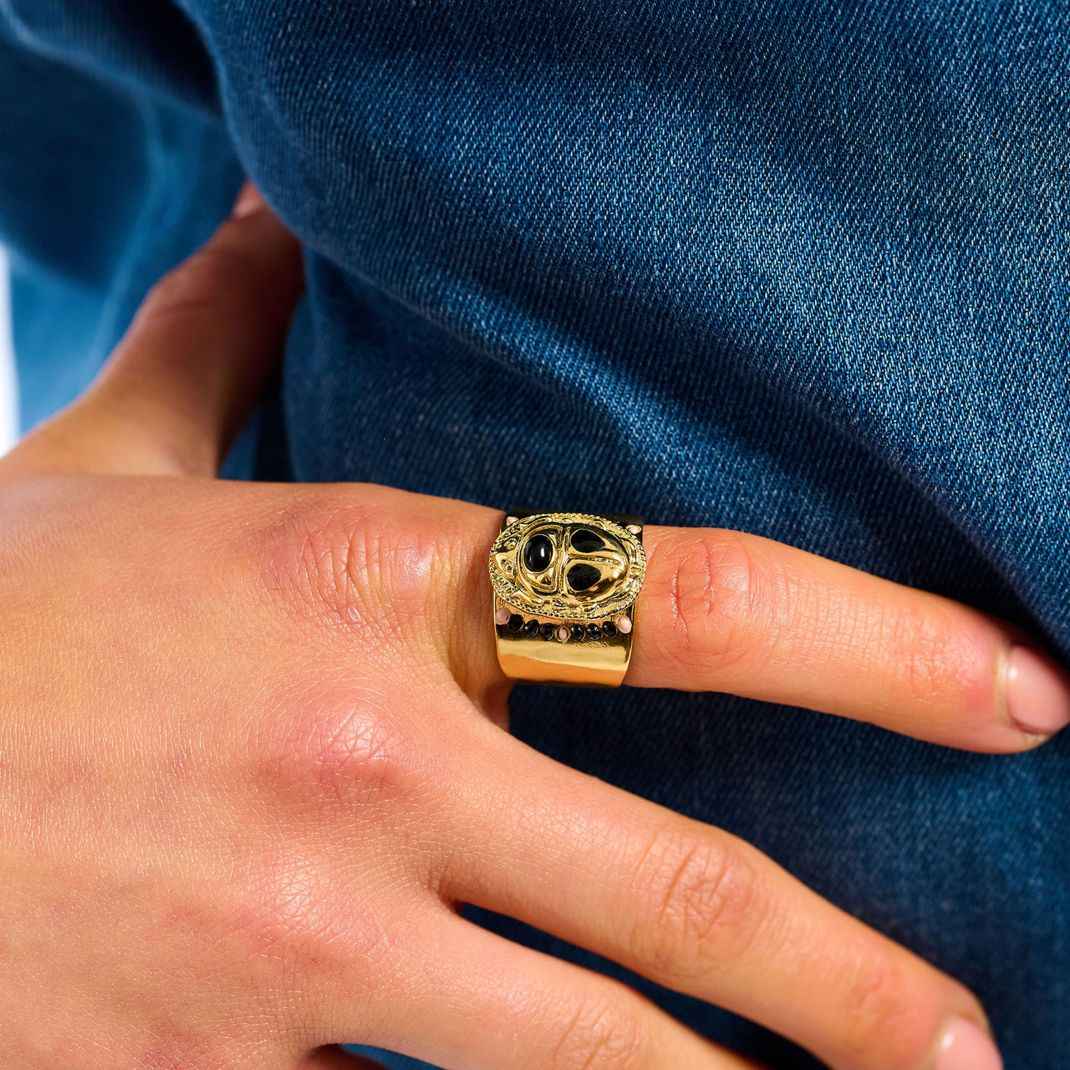 Gold ring with black stones on a person's finger against a blue background