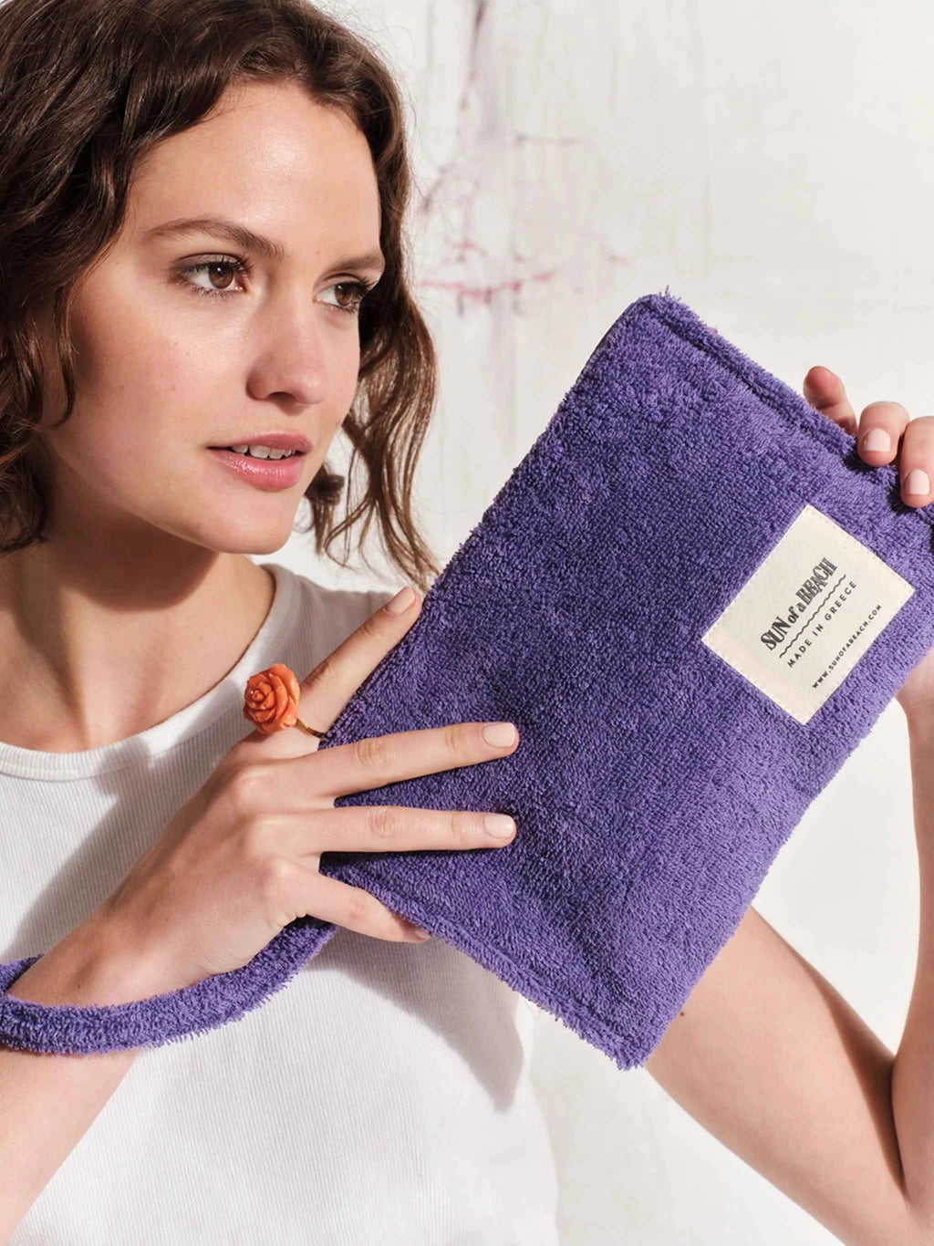 Woman holding a purple towel with a brand label against a neutral background