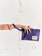 Person holding a purple pouch with a visible brand label on a light background