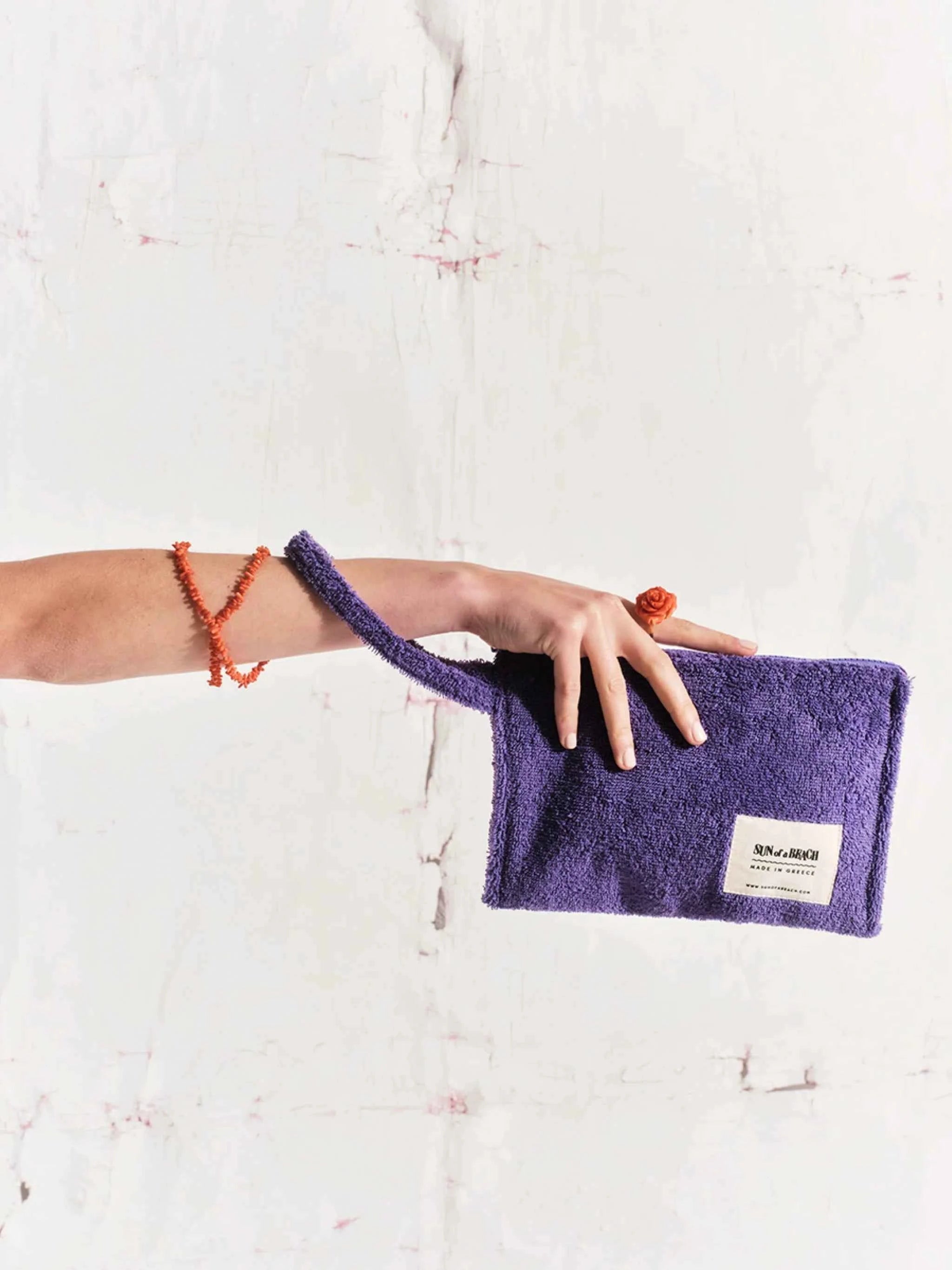 Person holding a purple pouch with a visible brand label on a light background
