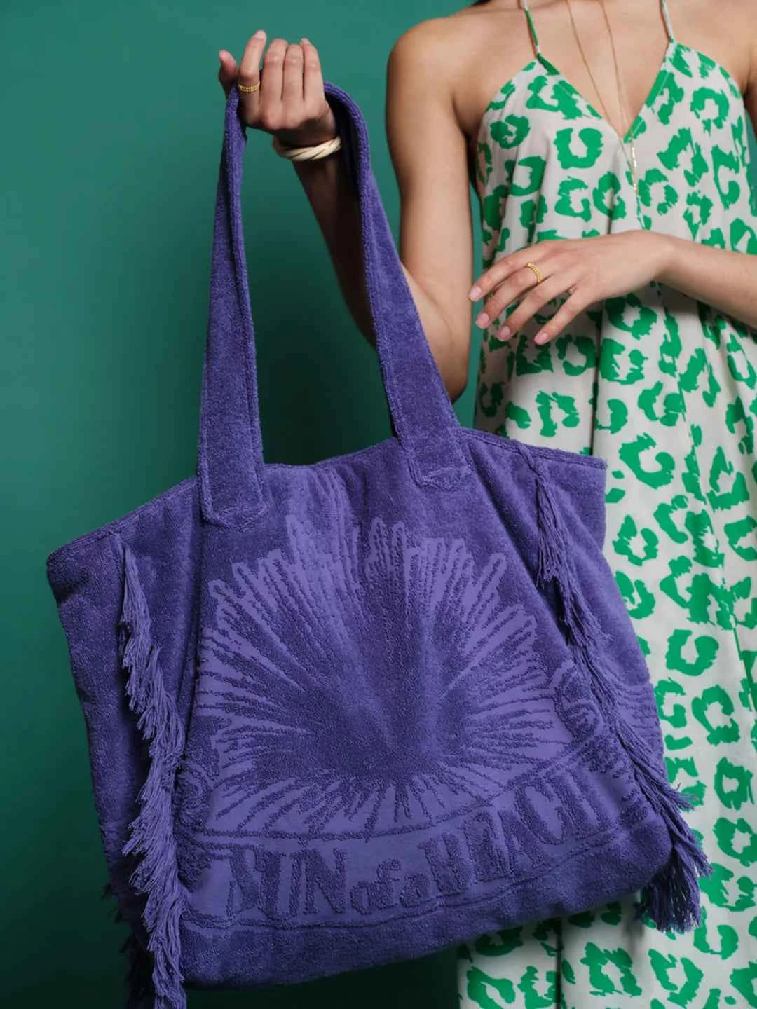 Person holding a purple tote bag with a green and white patterned dress in the background