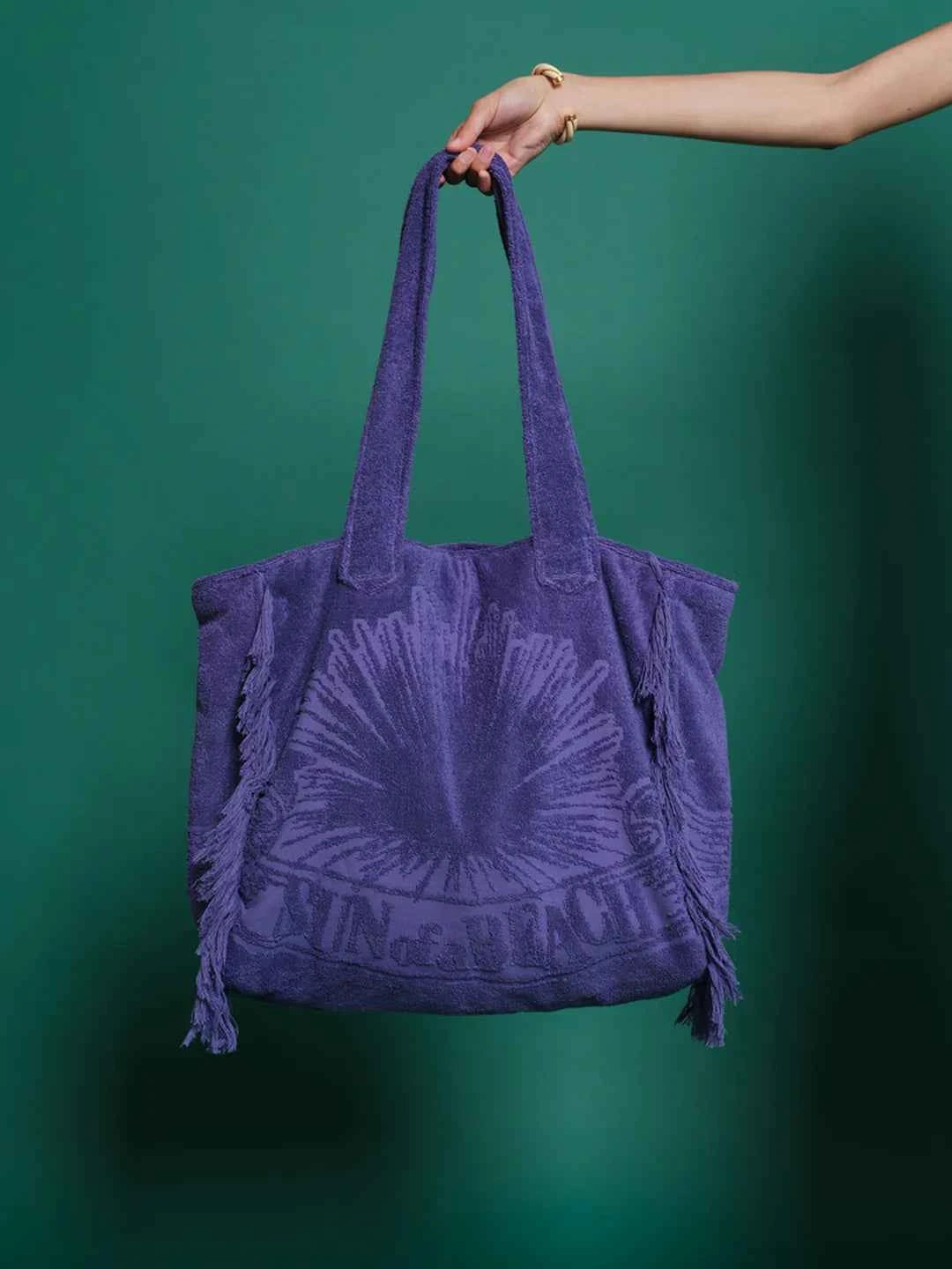 Purple tote bag with a sun design held against a green background