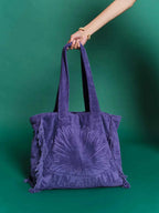 Purple tote bag with a sun design held by a hand against a green background