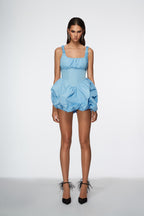 Woman wearing a light blue dress with ruffled details on a white background