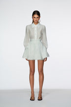 Woman wearing a white blouse and light green lace skirt on a white background
