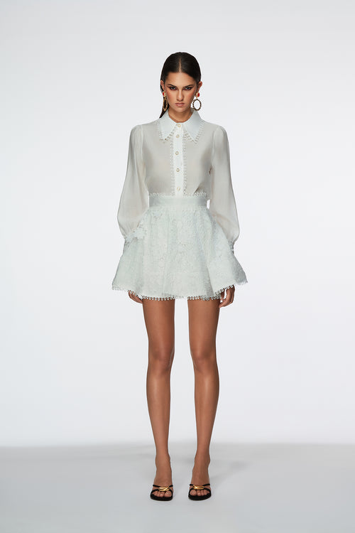 Woman wearing a white blouse and light green lace skirt on a white background