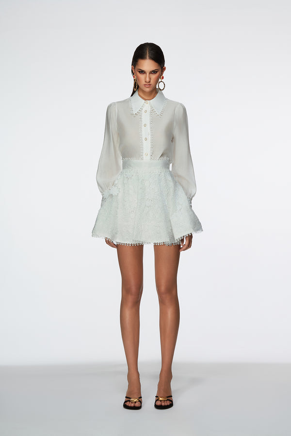 Woman wearing a white blouse and light green lace skirt on a white background