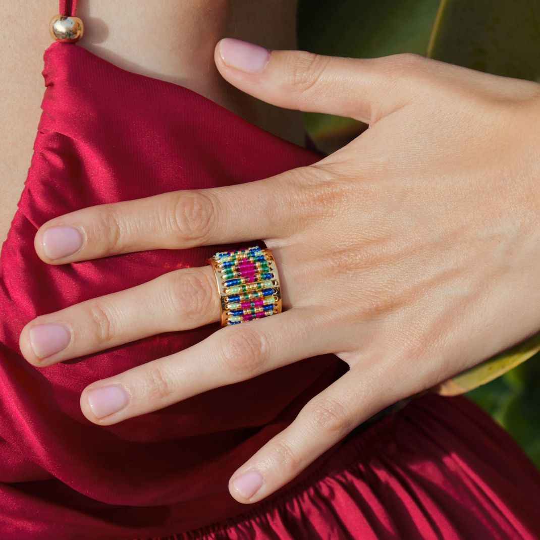 Hand wearing a colorful ring on a red fabric background