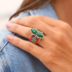 Hand wearing a colorful ring with green gemstones on denim fabric